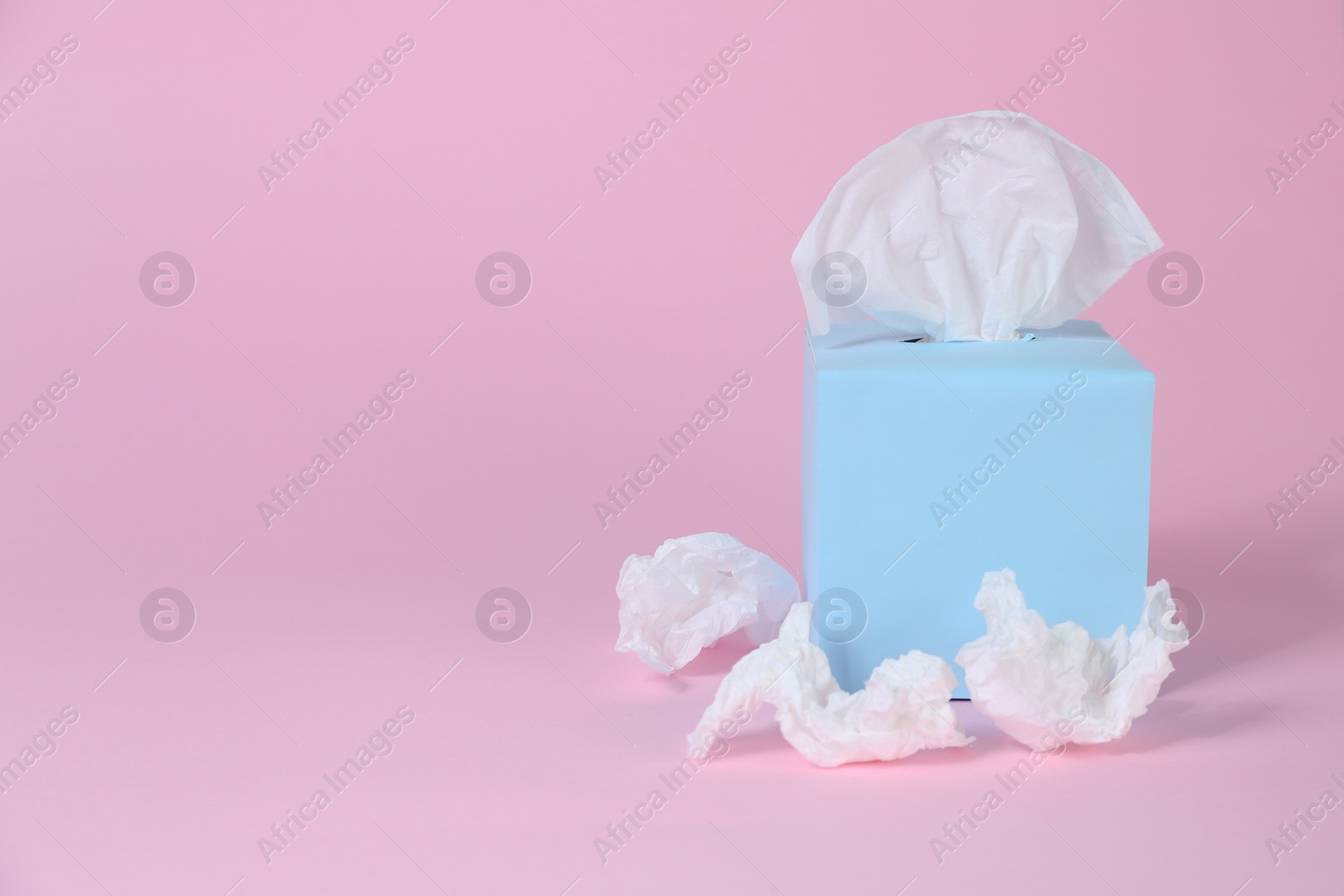 Photo of Box with paper tissues and used crumpled napkins on pink background, space for text