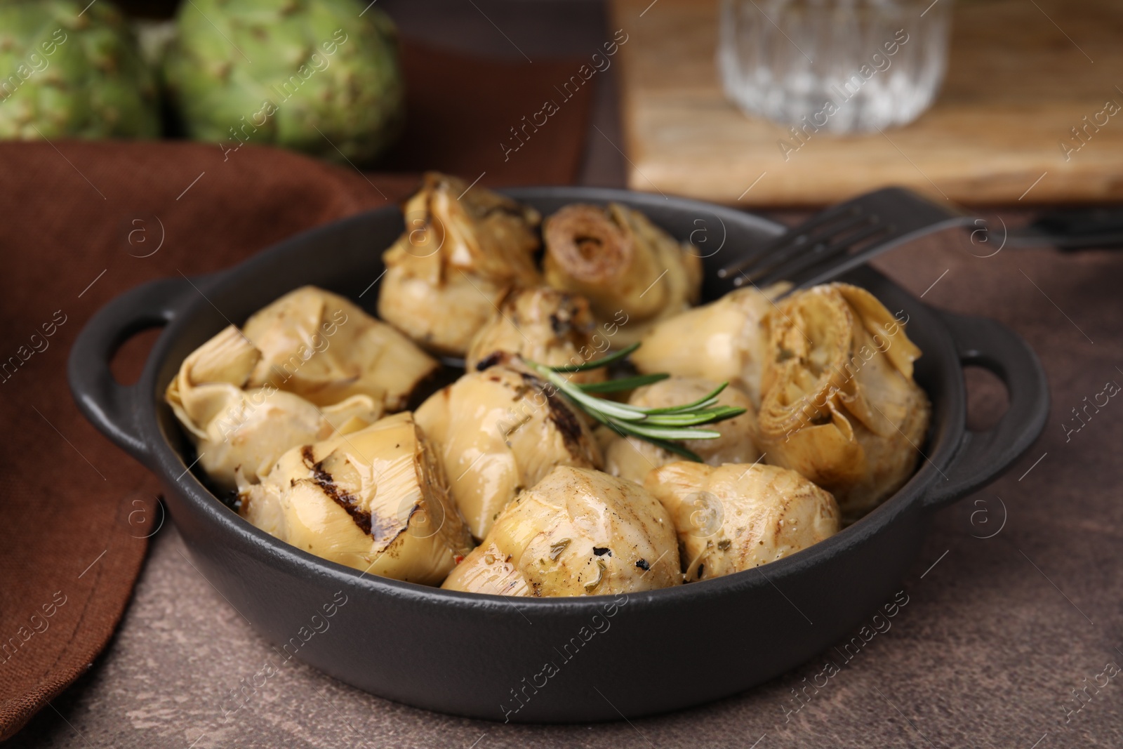 Photo of Delicious pickled artichokes with rosemary served on brown table, closeup