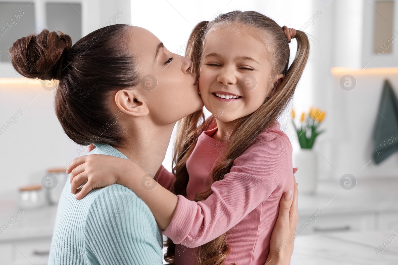 Photo of Happy mother kissing her cute daughter in kitchen