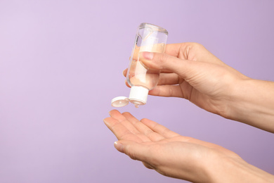 Photo of Woman applying antiseptic gel on lilac background, closeup