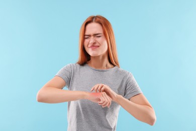 Photo of Suffering from allergy. Young woman scratching her arm on light blue background