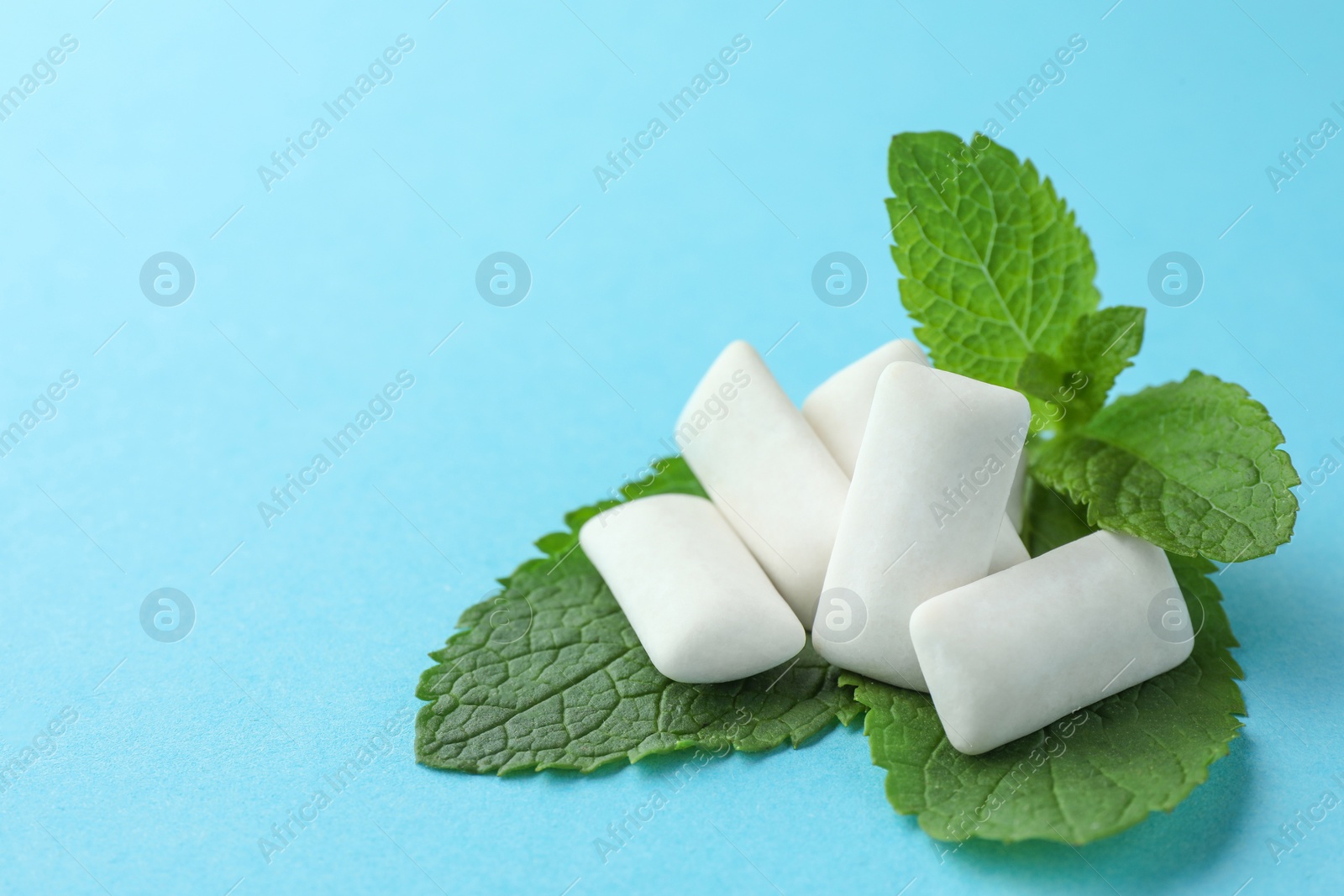 Photo of Tasty white chewing gums and mint leaves on light blue background, closeup. Space for text