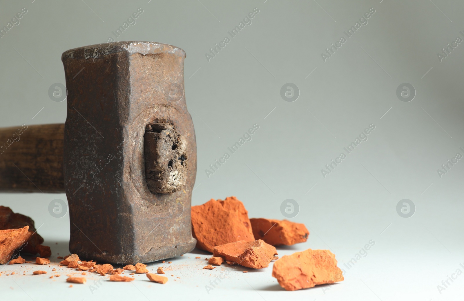 Photo of One sledgehammer and pieces of broken brick on grey background, closeup. Space for text