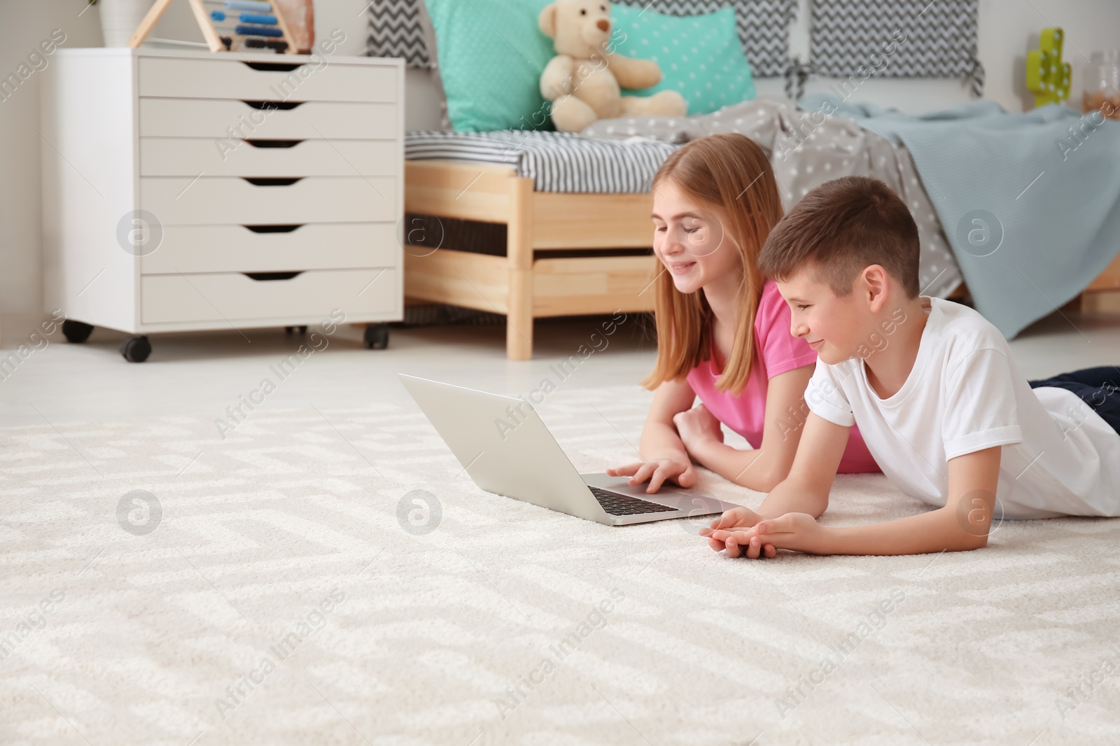 Photo of Teenage girl and her brother with laptop lying on cozy carpet at home