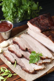 Photo of Pieces of baked pork belly served with sauce and parsley on black textured table, closeup