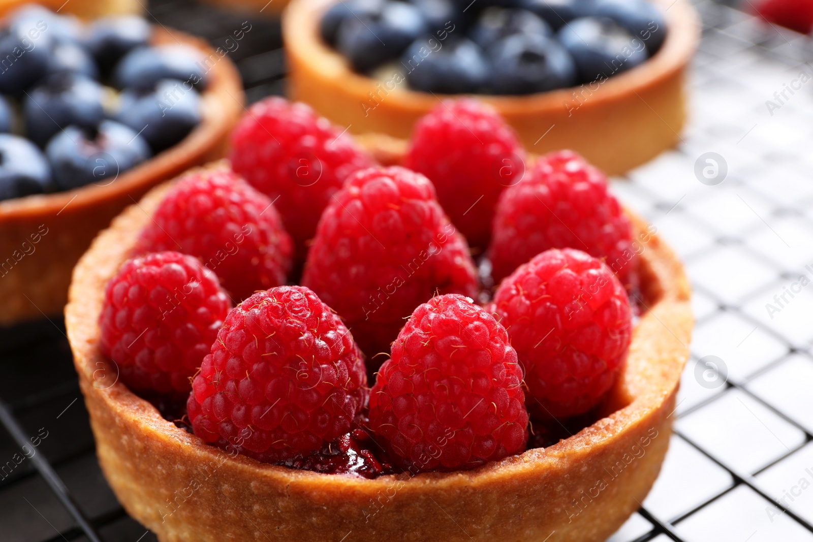 Photo of Tartlet with fresh raspberries on cooling rack, closeup. Delicious dessert