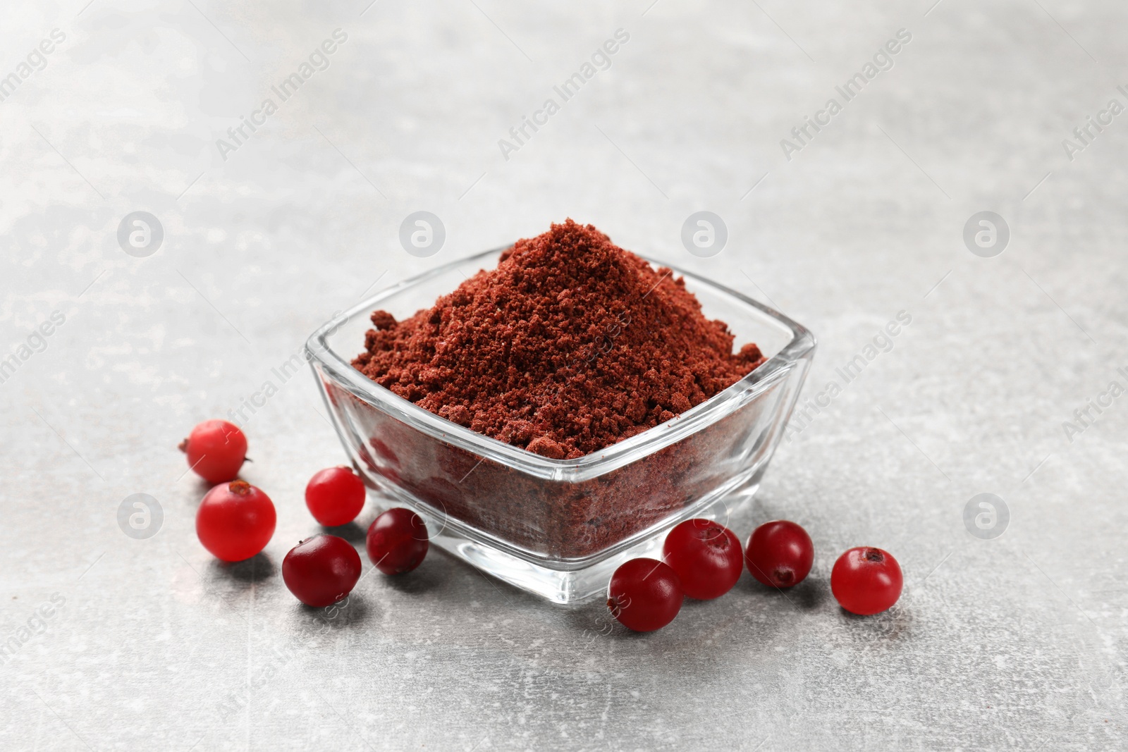 Photo of Cranberry powder in bowl and fresh berries on light grey table