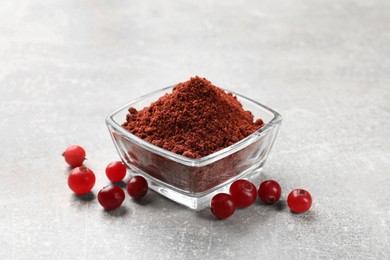 Photo of Cranberry powder in bowl and fresh berries on light grey table