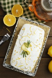 Photo of Tasty lemon cake with glaze and citrus fruits on wooden table, flat lay