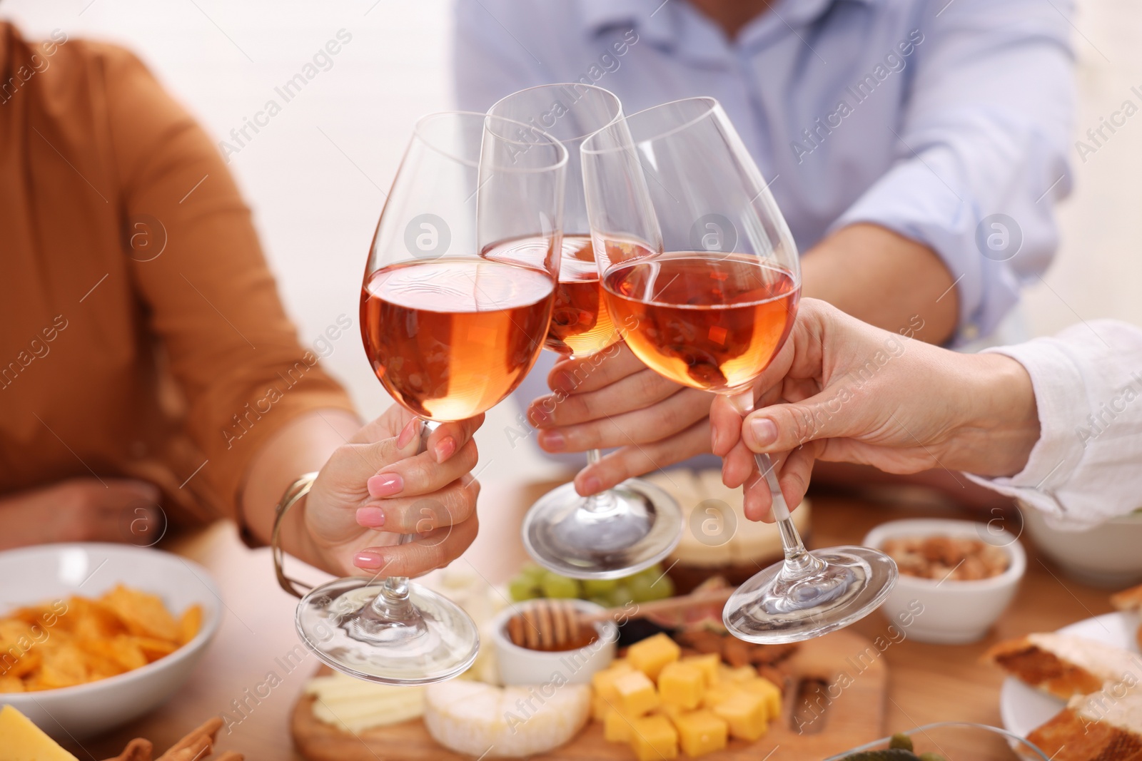 Photo of People clinking glasses with rose wine above table, closeup