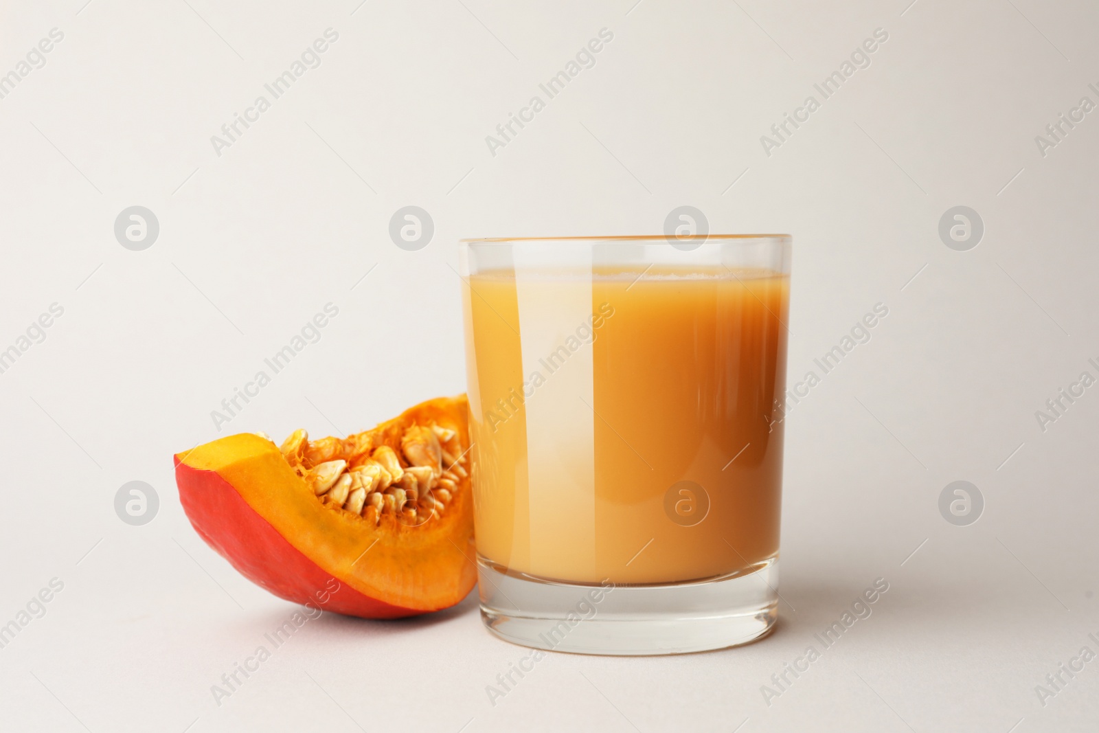 Photo of Tasty pumpkin juice in glass and cut pumpkin on light background