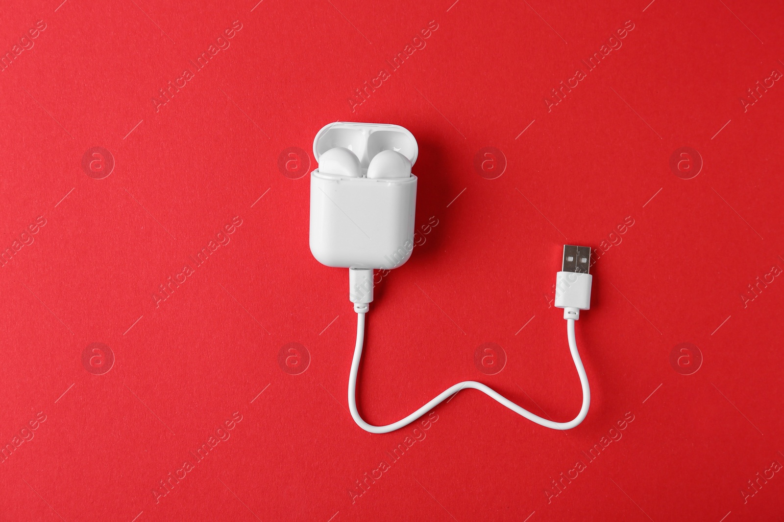 Photo of Modern wireless earphones in charging case with cable on red background, top view