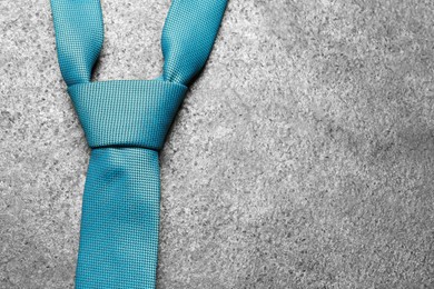 One blue necktie on grey textured background, top view. Space for text