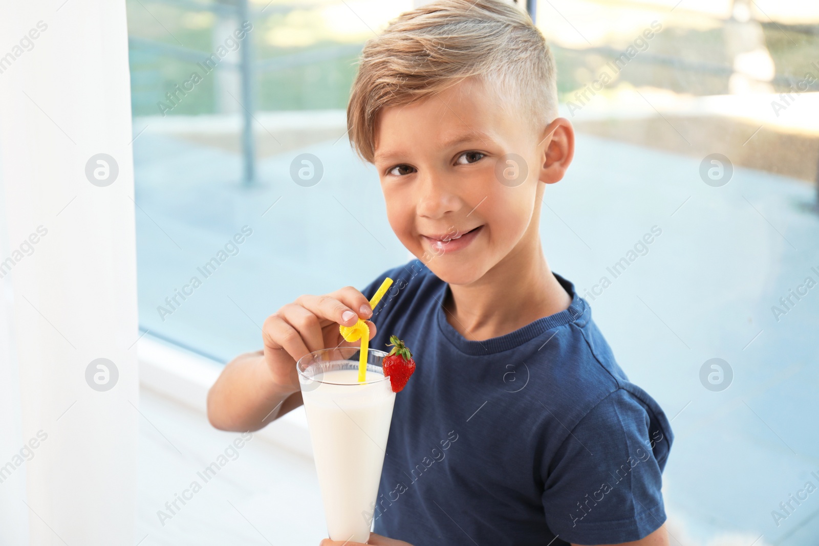 Photo of Little boy with glass of milk shake near window indoors