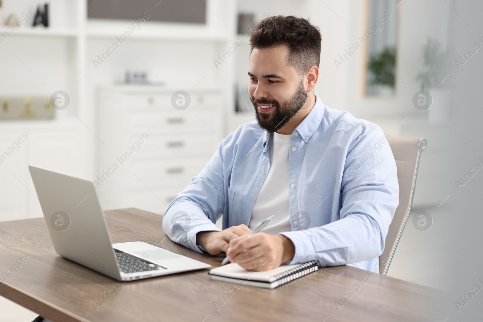 Photo of Young man watching webinar at table in room