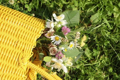 Photo of Yellow wicker bag with different wildflowers and herbs in meadow on sunny day, top view