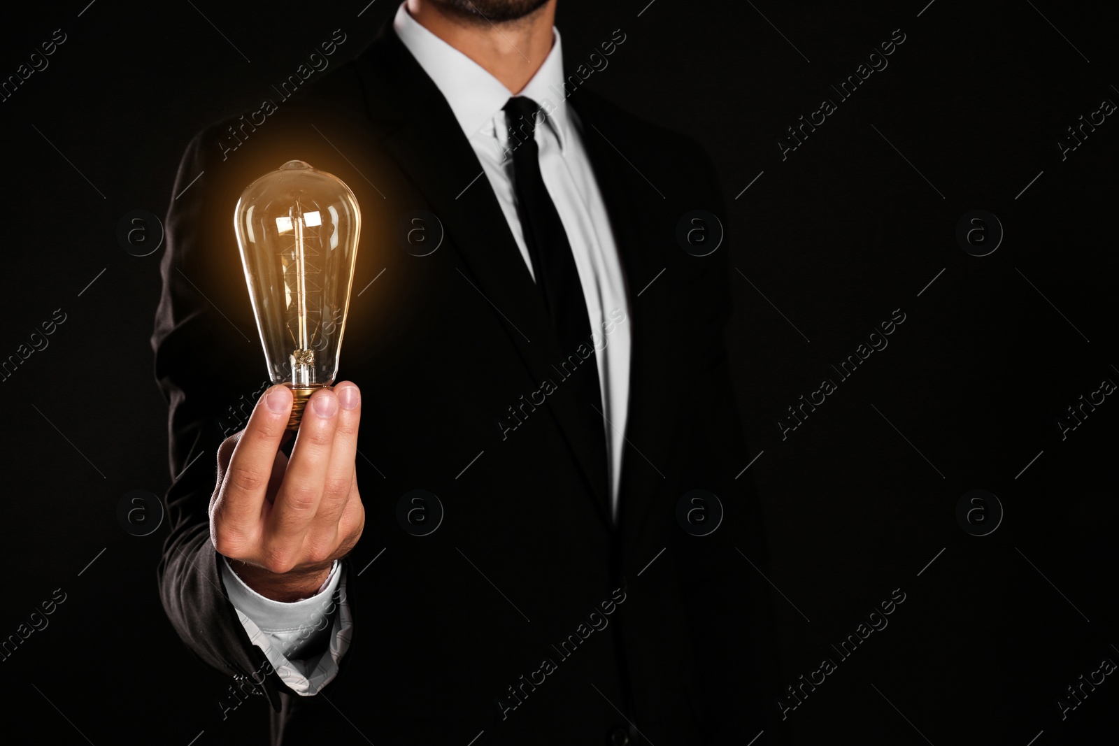 Photo of Businessman holding lamp bulb against dark background, closeup. Space for text