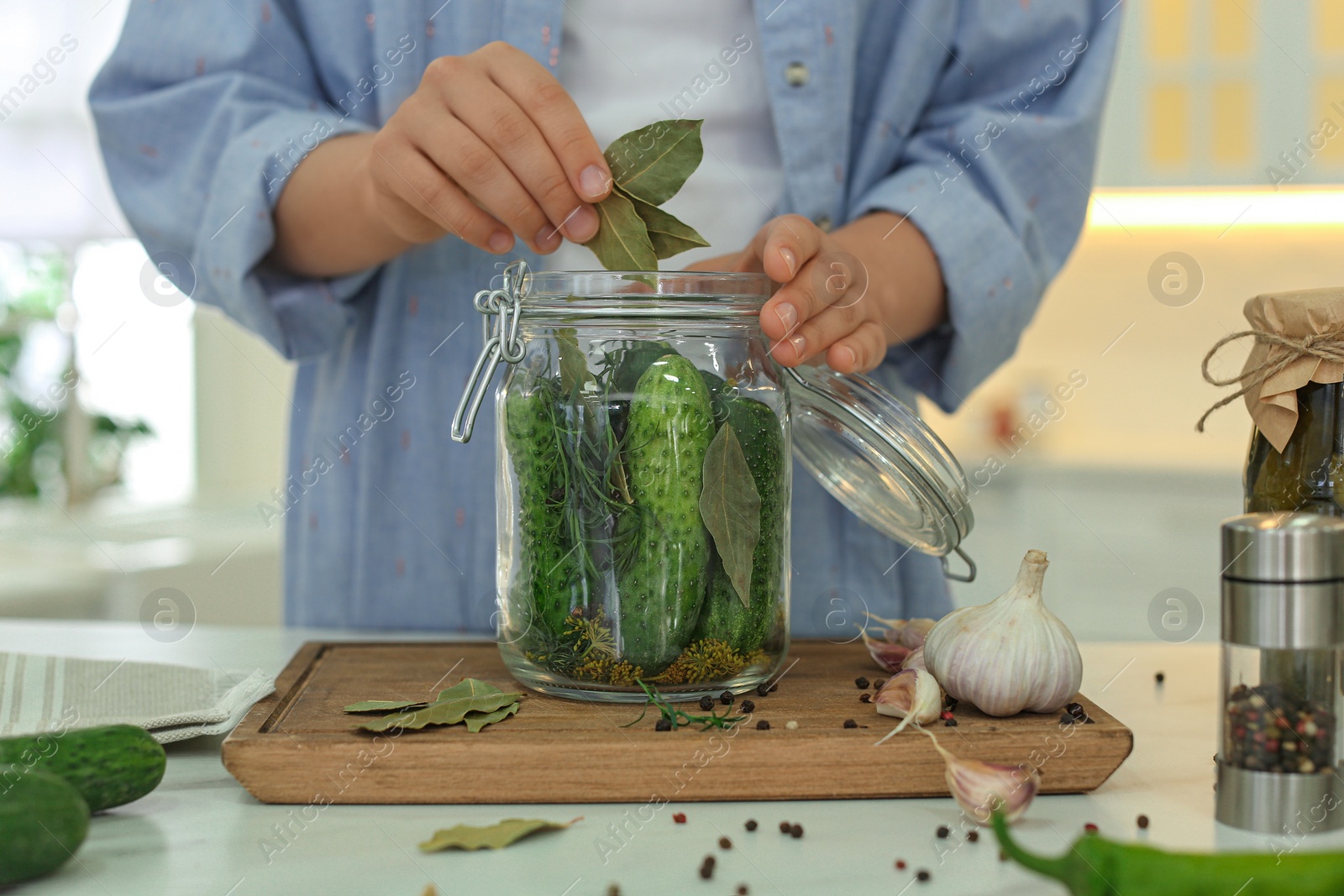 Photo of Woman putting bay leaves into pickling jar at table in kitchen, closeup