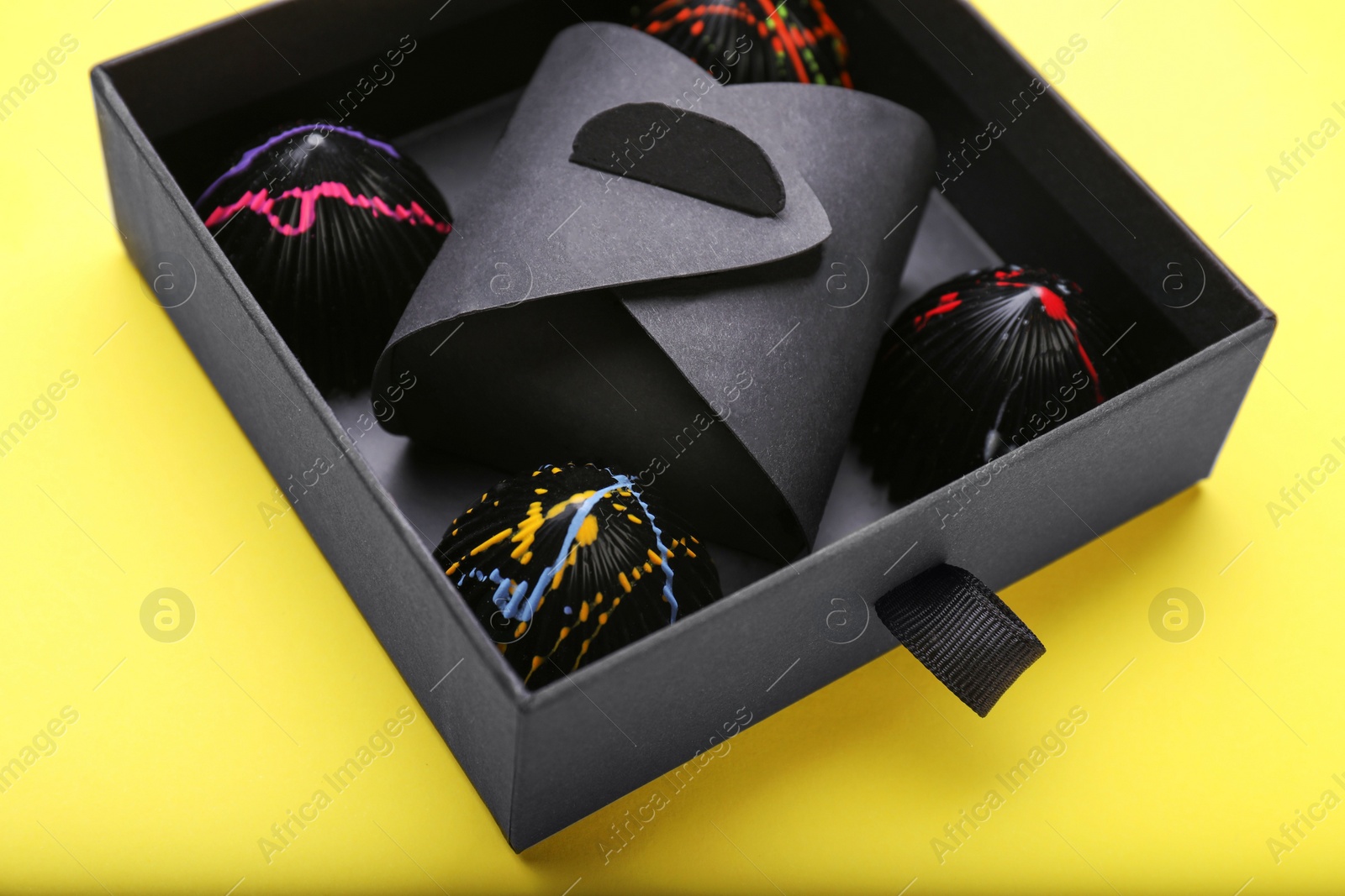 Photo of Box of tasty chocolate candies on yellow background, closeup