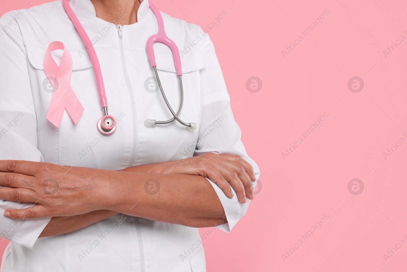 Photo of Doctor with pink ribbon and stethoscope on color background, closeup and space for text. Breast cancer awareness