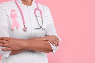 Doctor with pink ribbon and stethoscope on color background, closeup and space for text. Breast cancer awareness