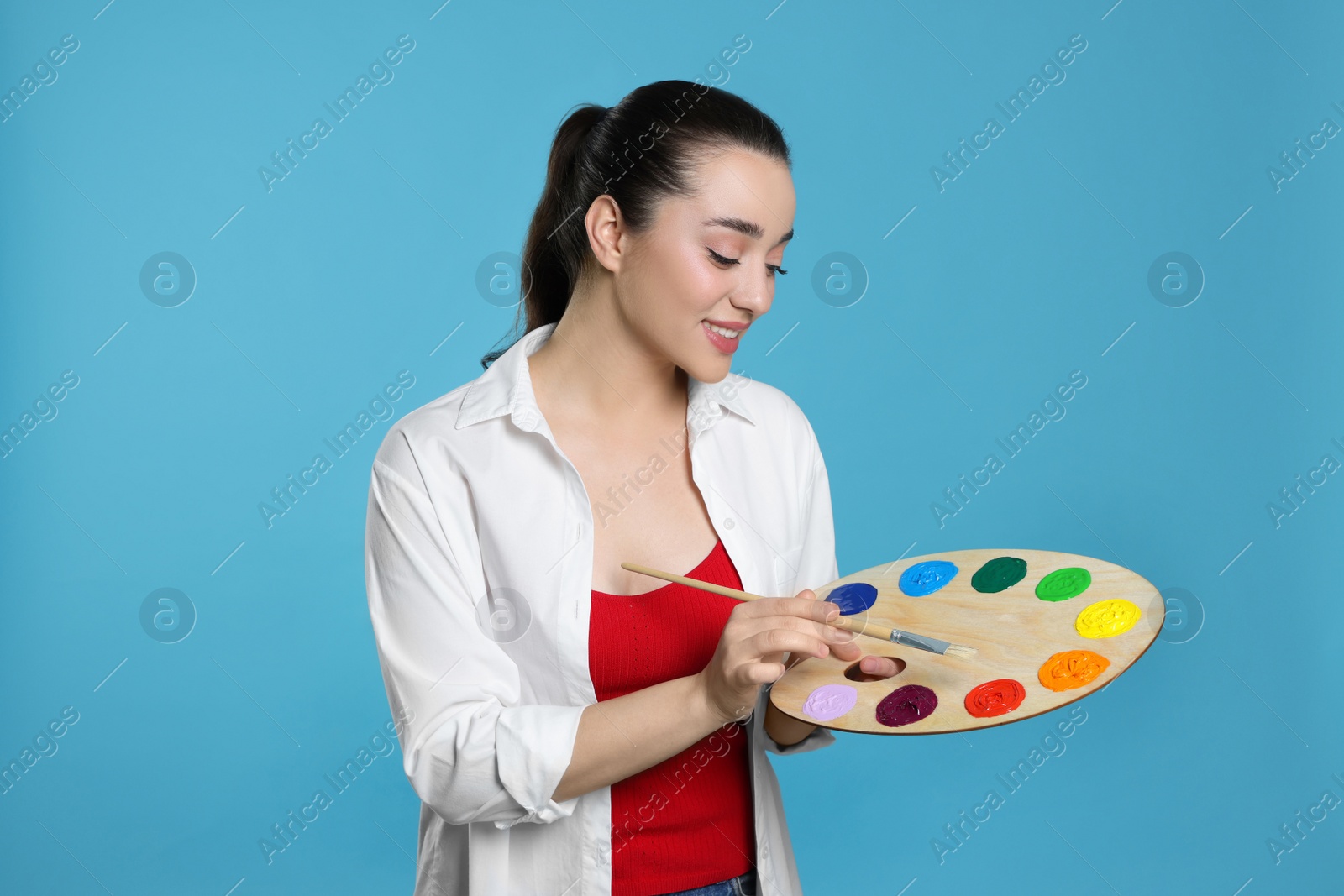 Photo of Woman with painting tools on light blue background. Young artist