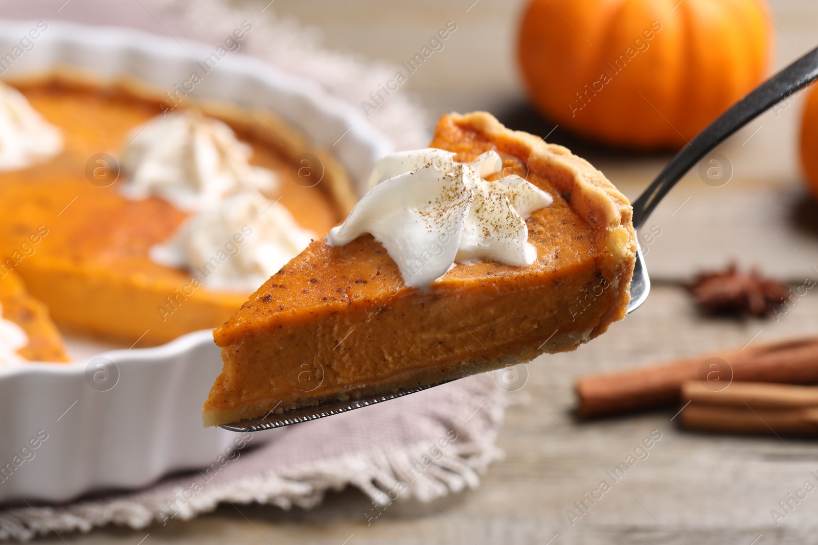 Photo of Piece of delicious pumpkin pie with whipped cream on server over table, closeup