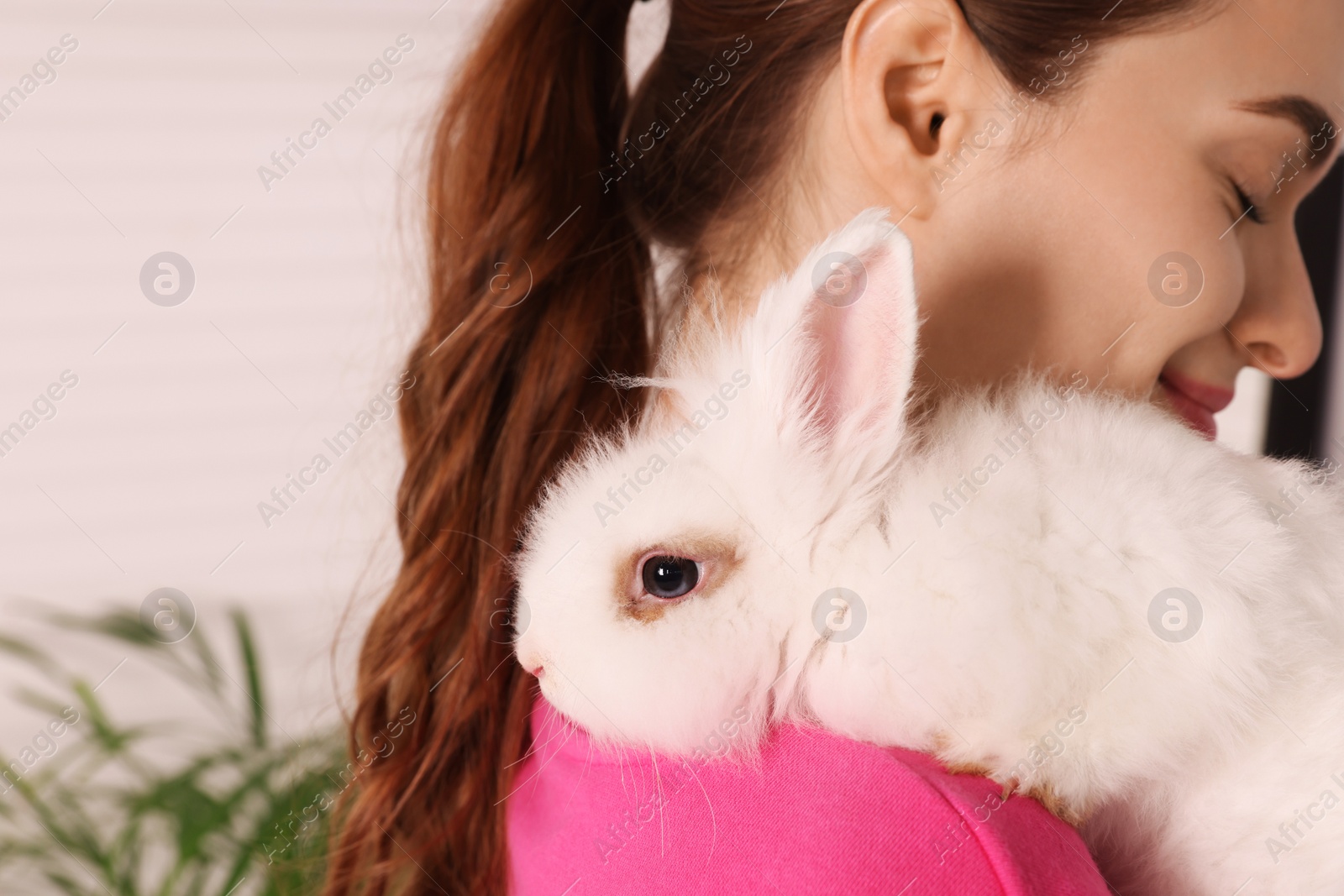 Photo of Woman with fluffy white rabbit indoors, closeup and space for text. Cute pet