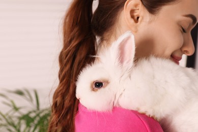 Photo of Woman with fluffy white rabbit indoors, closeup and space for text. Cute pet