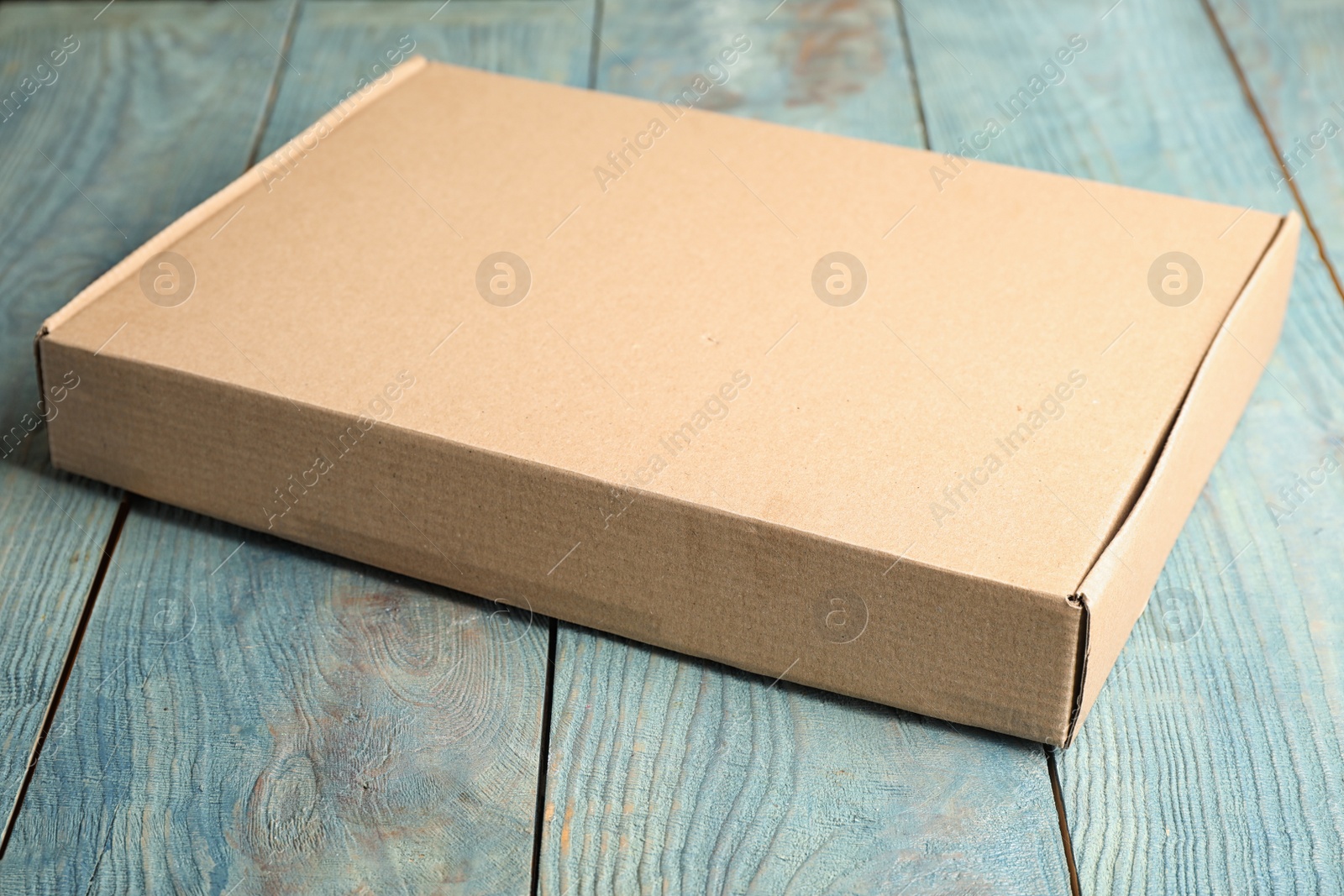 Photo of Closed cardboard box on light blue wooden table