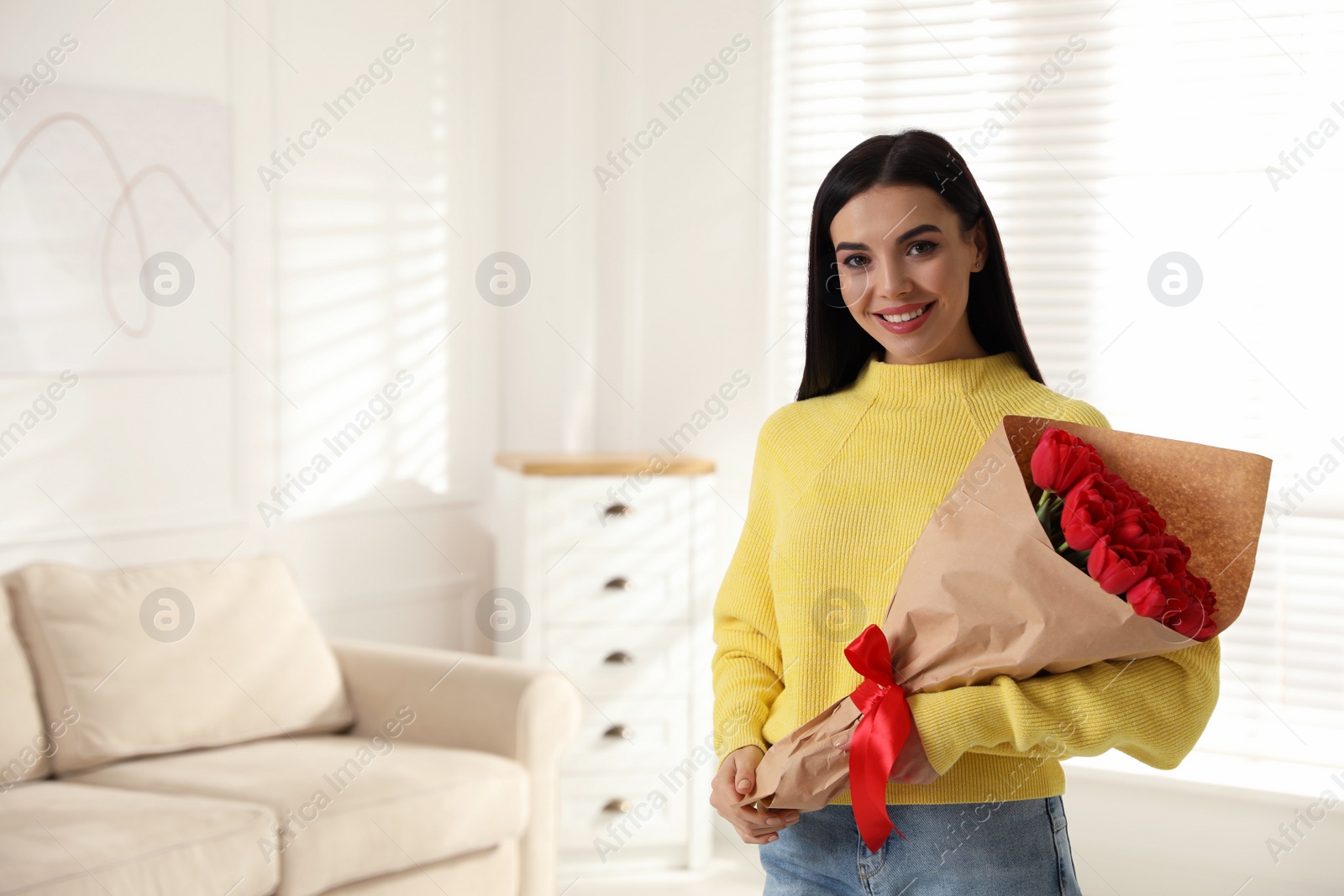 Photo of Happy woman with red tulip bouquet at home, space for text. 8th of March celebration