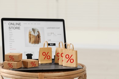 Image of Discount offer. Mini shopping bags and boxes with percent signs, laptop on table