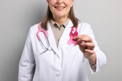 Photo of Mammologist with pink ribbon on gray background, closeup. Breast cancer awareness