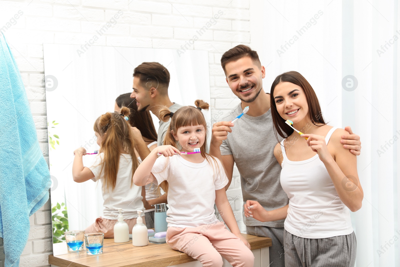 Photo of Little girl and her parents brushing teeth together in bathroom at home. Space for text