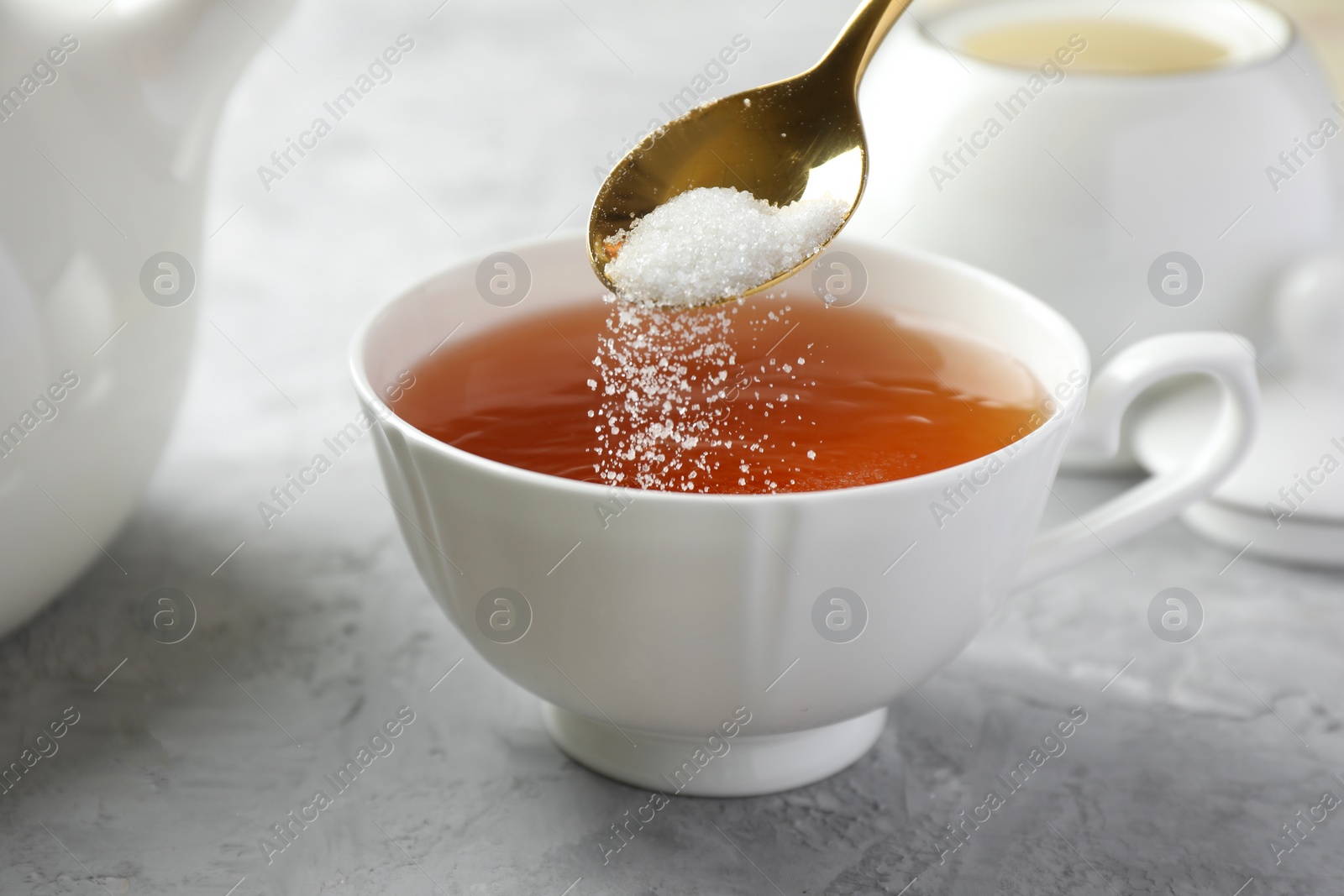 Photo of Adding sugar into cup of tea at grey textured table, closeup