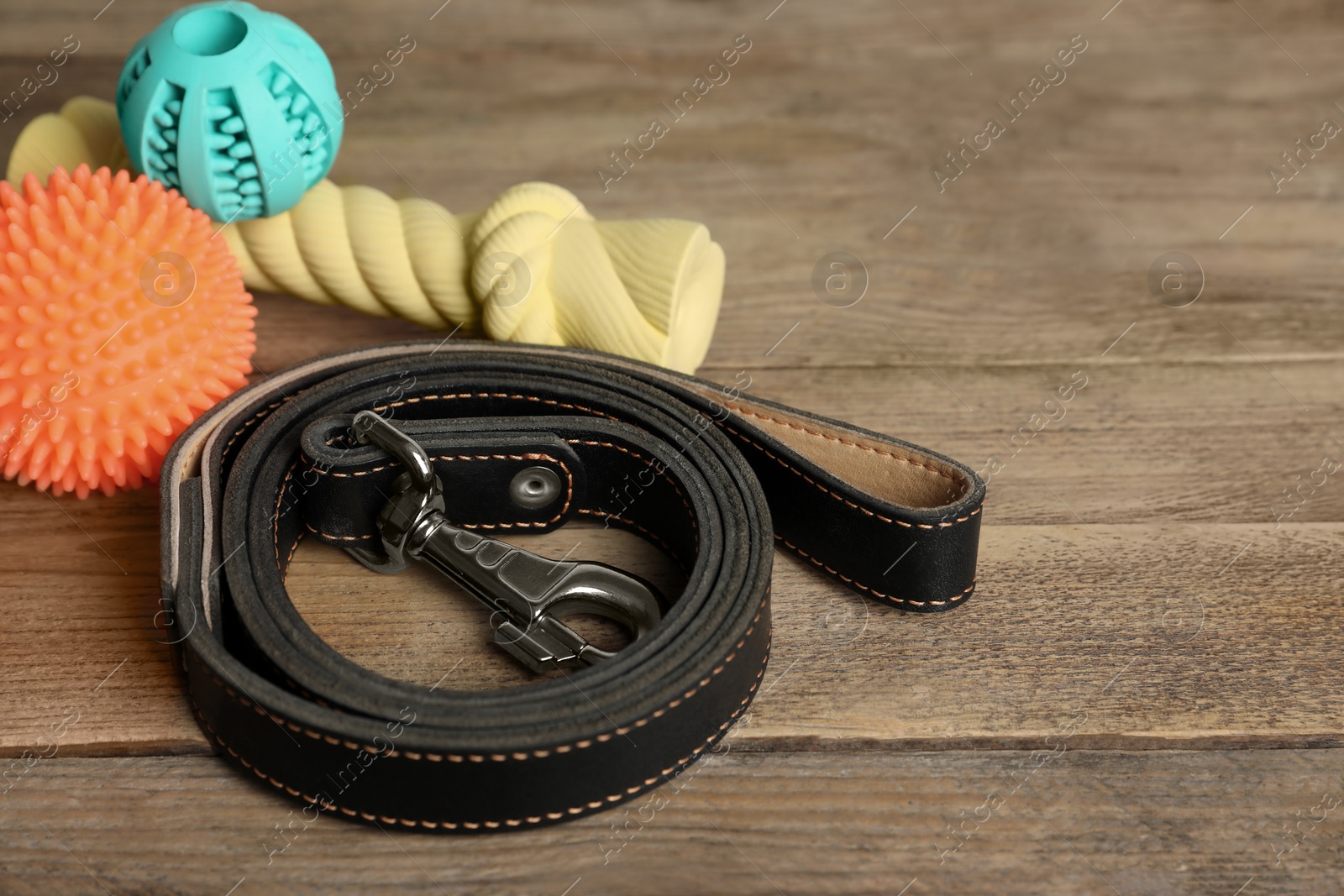 Photo of Black leather dog leash and toys on wooden background, closeup