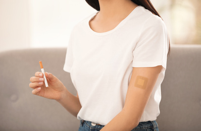 Photo of Young woman with nicotine patch and cigarette at home, closeup