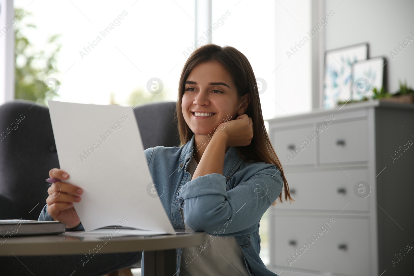 Photo of Young woman reading paper letter at home
