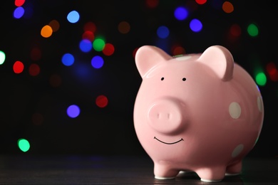 Photo of Piggy bank on wooden table against blurred Christmas lights, space for text