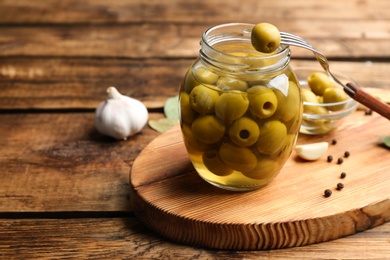 Photo of Glass jar of pickled olives on wooden table. Space for text