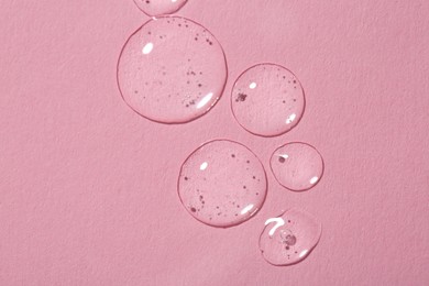 Drops of cosmetic serum on pink background, top view