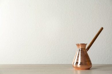 Photo of Copper turkish coffee pot on wooden table against white background, space for text