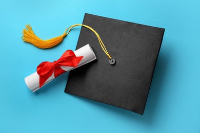 Photo of Graduation hat and diploma on light blue background, flat lay