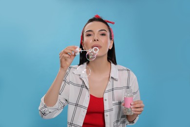 Young woman blowing soap bubbles on light blue background