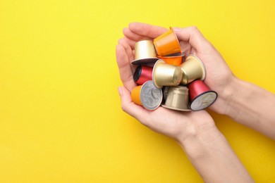 Woman holding heap of coffee capsules on yellow background, top view. Space for text