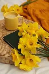 Bouquet of beautiful daffodils, book and coffee on bed