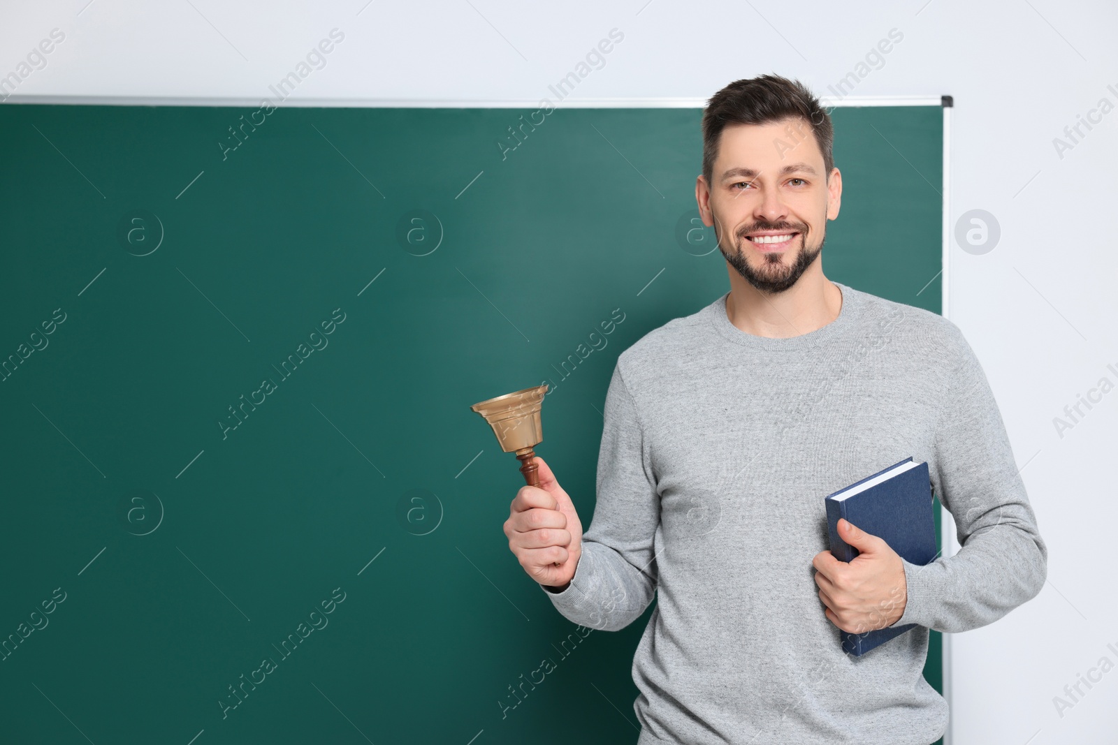 Photo of Teacher with school bell near chalkboard indoors. Space for text