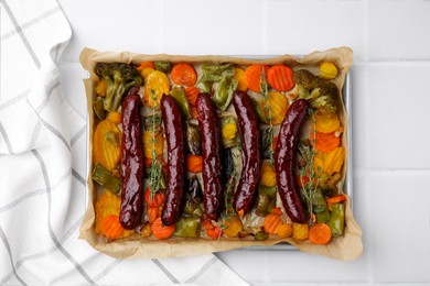 Baking tray with delicious smoked sausages and vegetables on white table, top view