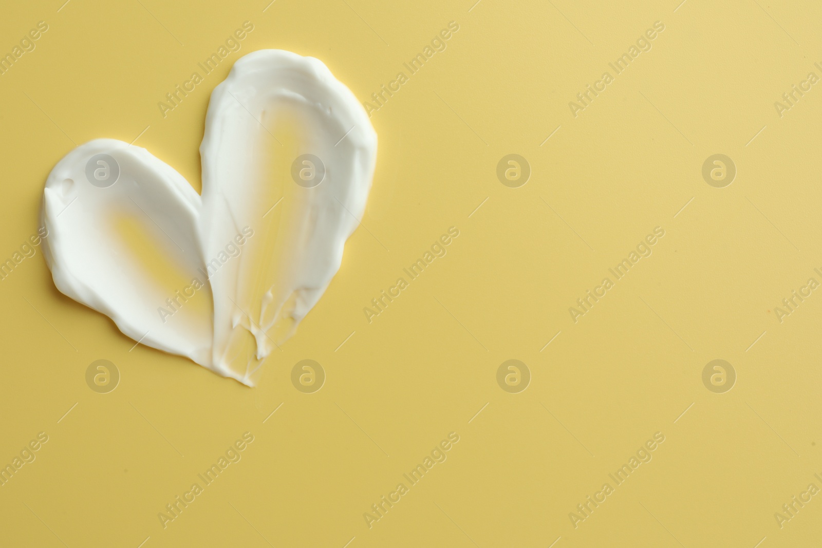 Photo of Samples of face cream in shape of heart on yellow background, top view. Space for text