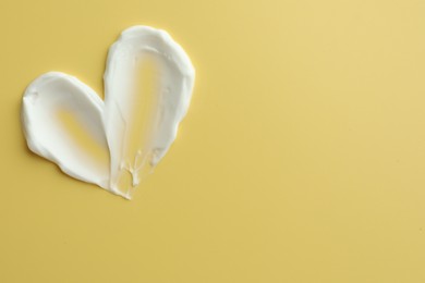 Samples of face cream in shape of heart on yellow background, top view. Space for text